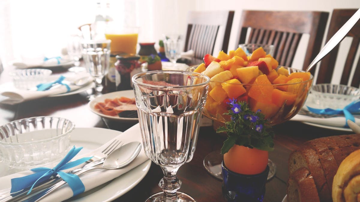 A beautifully set dining table featuring a colorful fruit salad in a cozy indoor setting.